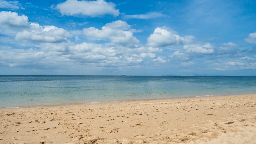 Plage de sable clair et déserte au bord d'une mer turquoise, sous un ciel bleu nuageux