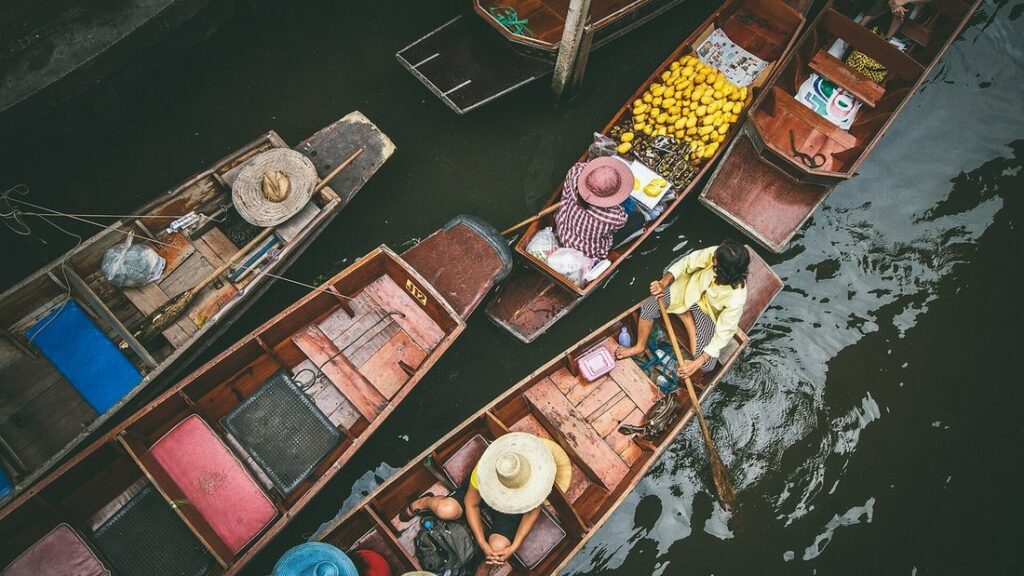Vue aérienne de barques en bois chargées de fruits sur un canal, avec des vendeurs coiffés de chapeaux