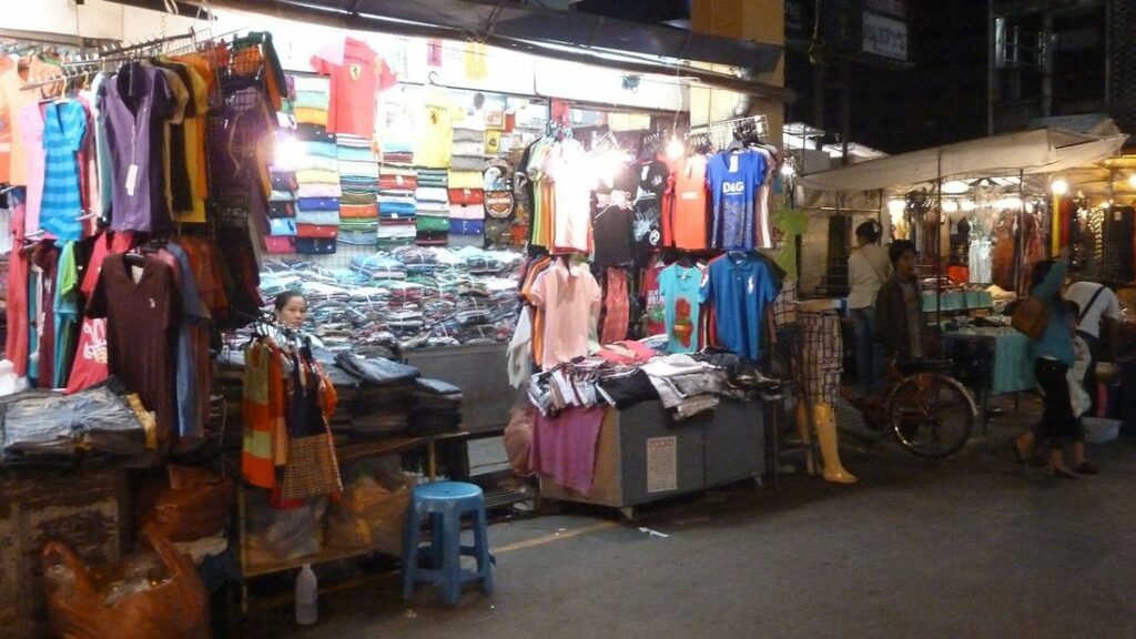 Étals de vêtements colorés sous les lumières d'un marché de rue à Chiang Mai