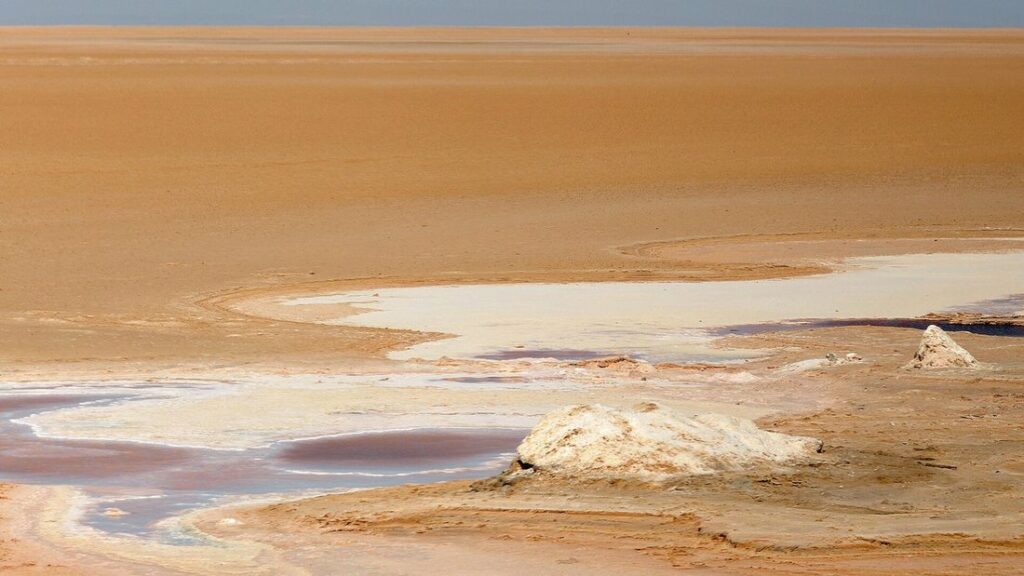 Étendue plate de sel et de sable clair, avec une nappe d'eau peu profonde aux reflets rosés