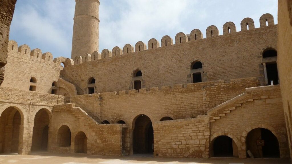 Cour de pierre ocre à arcades surmontée de murs crénelés et d'une tour de guet, dans le ribat de Sousse