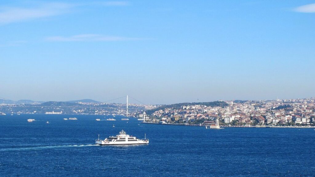 Un ferry blanc sur les eaux bleues du Bosphore, avec un pont suspendu et les quartiers de la rive au loin