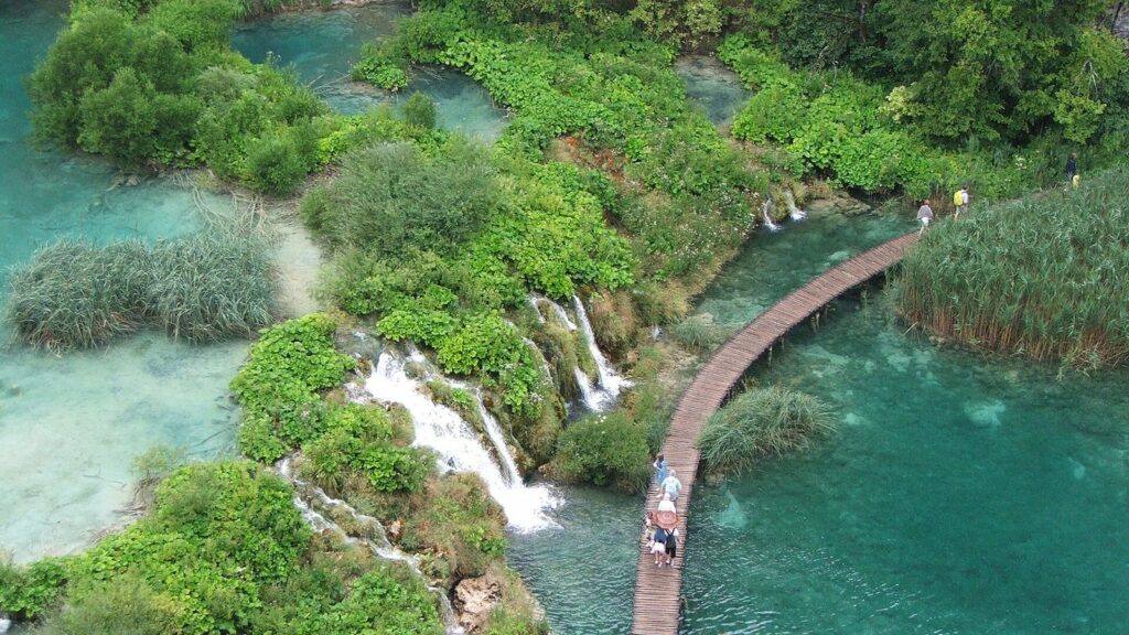 Passerelle de bois au-dessus des lacs turquoise de Plitvice, avec des visiteurs et de petites cascades