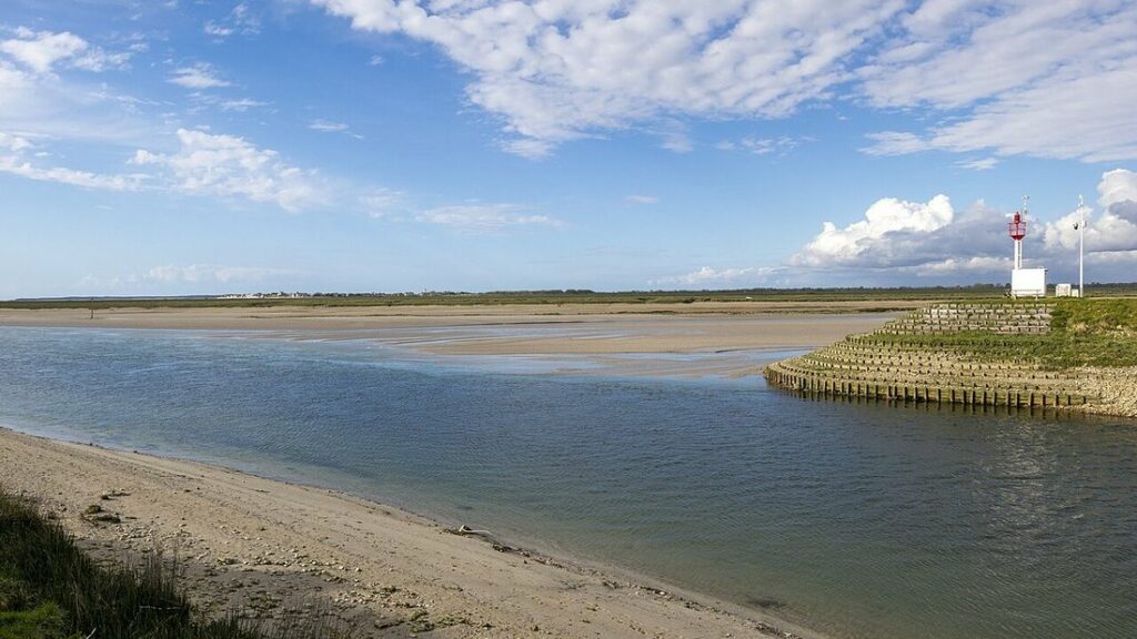Chenal de la baie de Somme entre une plage de sable et des bancs découverts, avec un petit feu rouge sur une digue