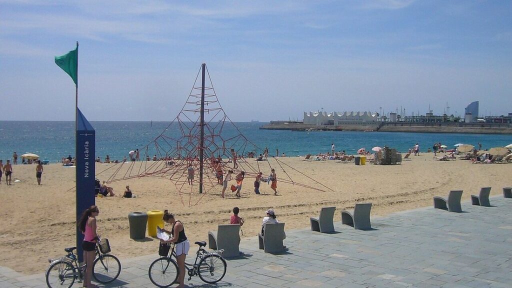 Pyramide de cordes pour enfants sur le sable de la plage de la Nova Icària, avec des vélos sur la promenade