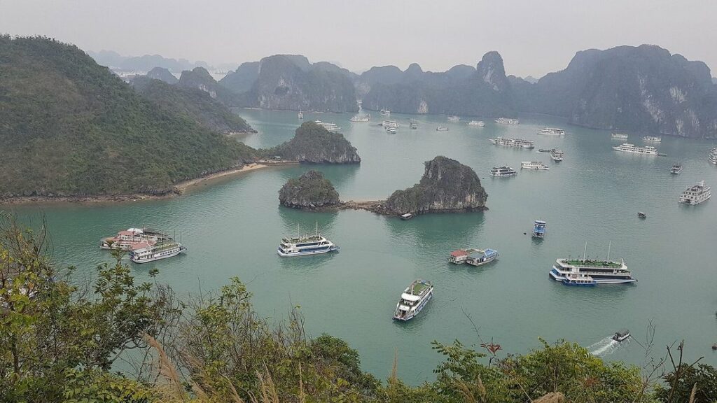 Rochers calcaires couverts de végétation et bateaux sur l'eau verte de la baie d'Halong, vus d'en haut
