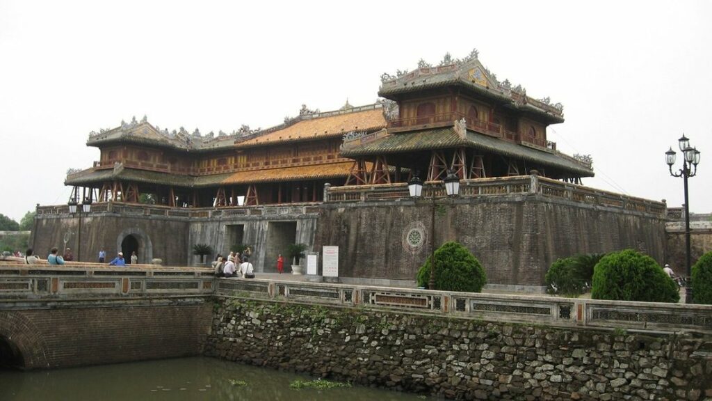 La porte Ngo Mon et son pavillon à toits de tuiles, derrière un pont de pierre au-dessus des douves