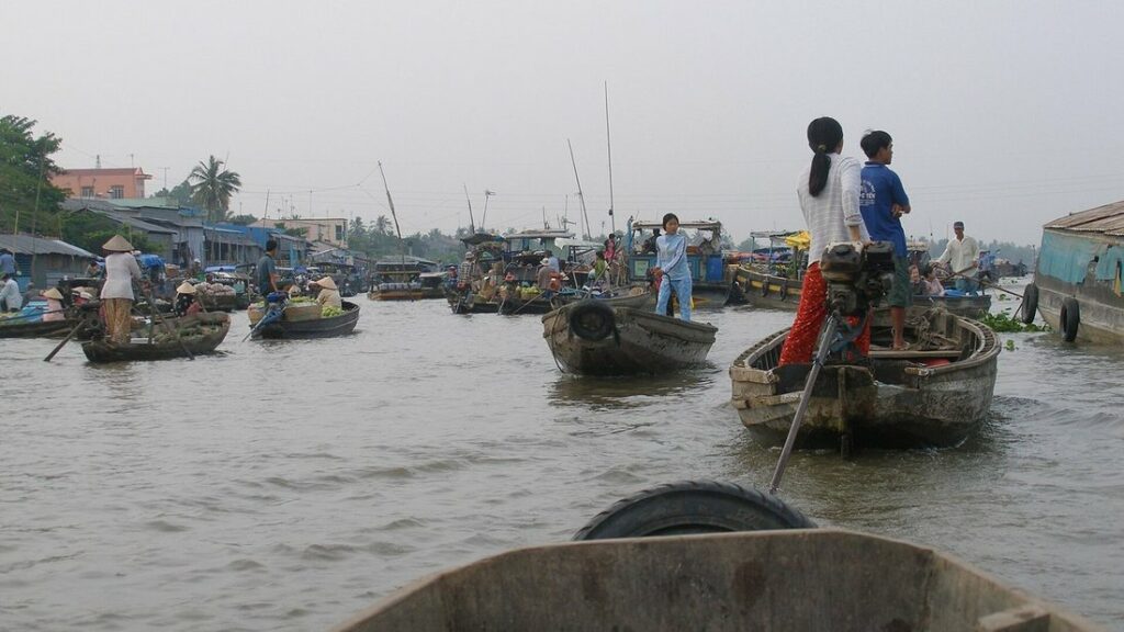 Barques en bois chargées de marchandises sur l'eau brune d'un marché flottant de Can Tho, vues depuis une autre barque