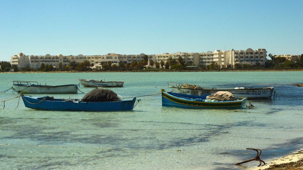 Barques de pêche amarrées dans l'eau turquoise peu profonde de Djerba, devant une rangée de bâtiments blancs
