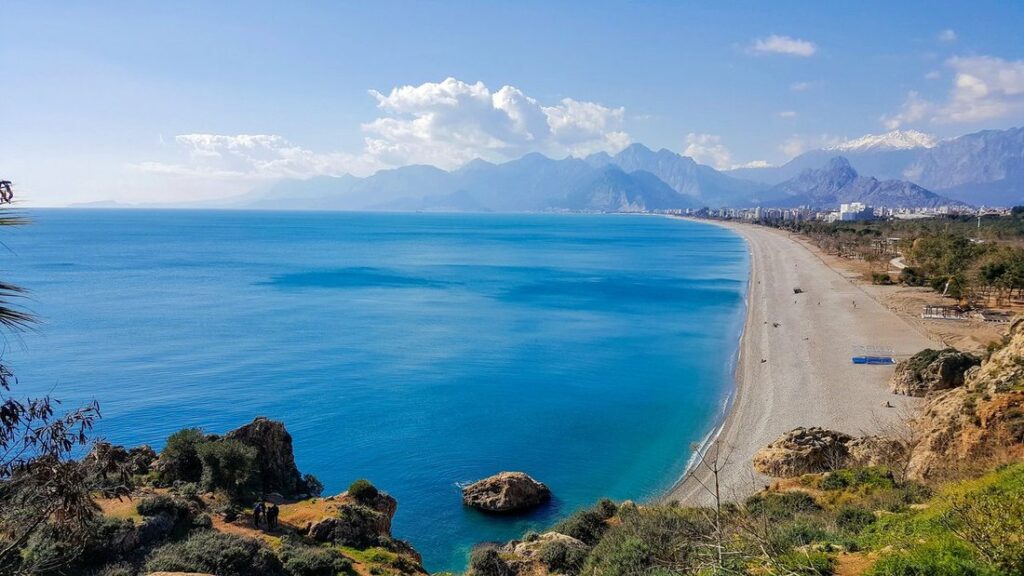 Longue plage de Konyaaltı à Antalya vue depuis les falaises, mer bleu intense et chaîne de montagnes au fond