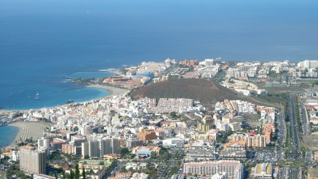 Vue aérienne de la côte sud de Tenerife : plages, immeubles blancs de la station et cône volcanique brun