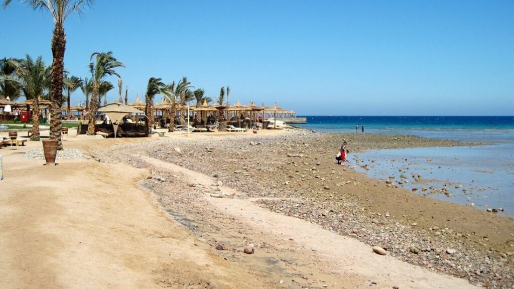 Plage de la mer Rouge à Hurghada : palmiers, parasols de paille et eau bleu profond
