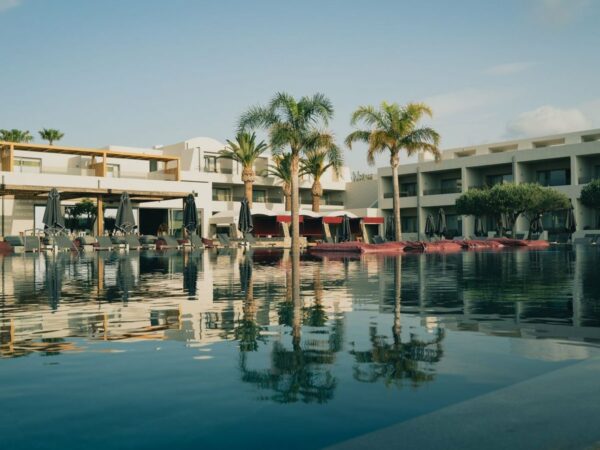 Bassin calme d'un hôtel-club reflétant des bâtiments blancs, des palmiers et des transats aux parasols fermés