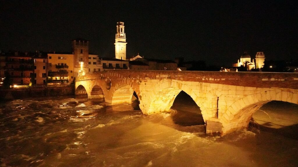 Le Ponte Pietra de Vérone éclairé de nuit, ses arches de pierre claire au-dessus de l'Adige et un campanile en arrière-plan