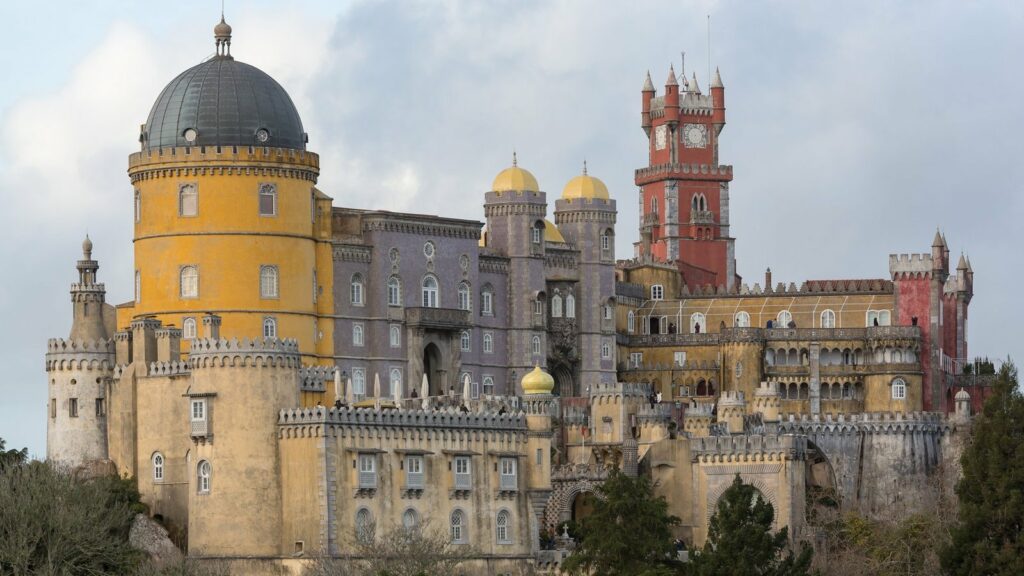 Le palais de Pena à Sintra, avec sa tour rouge, sa rotonde jaune et ses murs crénelés dressés sur la colline boisée