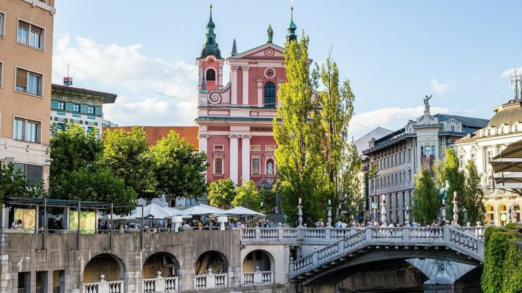 Triple pont de Ljubljana au-dessus de la Ljubljanica, avec l'église franciscaine rose et des terrasses au bord de l'eau