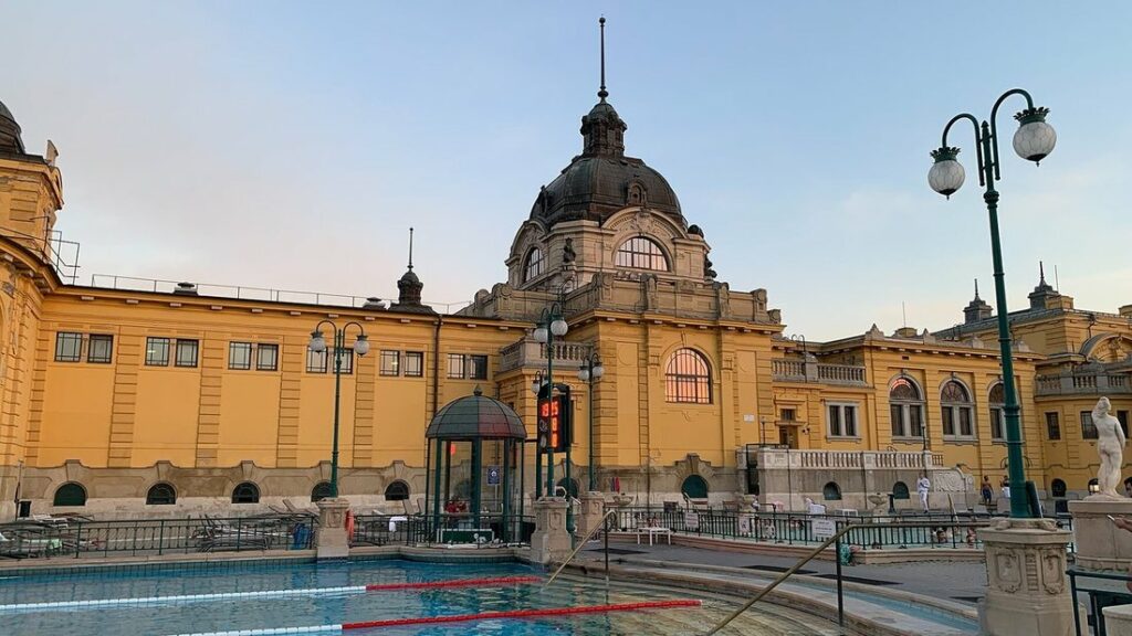 Façade jaune des thermes Széchenyi de Budapest, avec sa coupole, ses lampadaires verts et un bassin extérieur au premier plan
