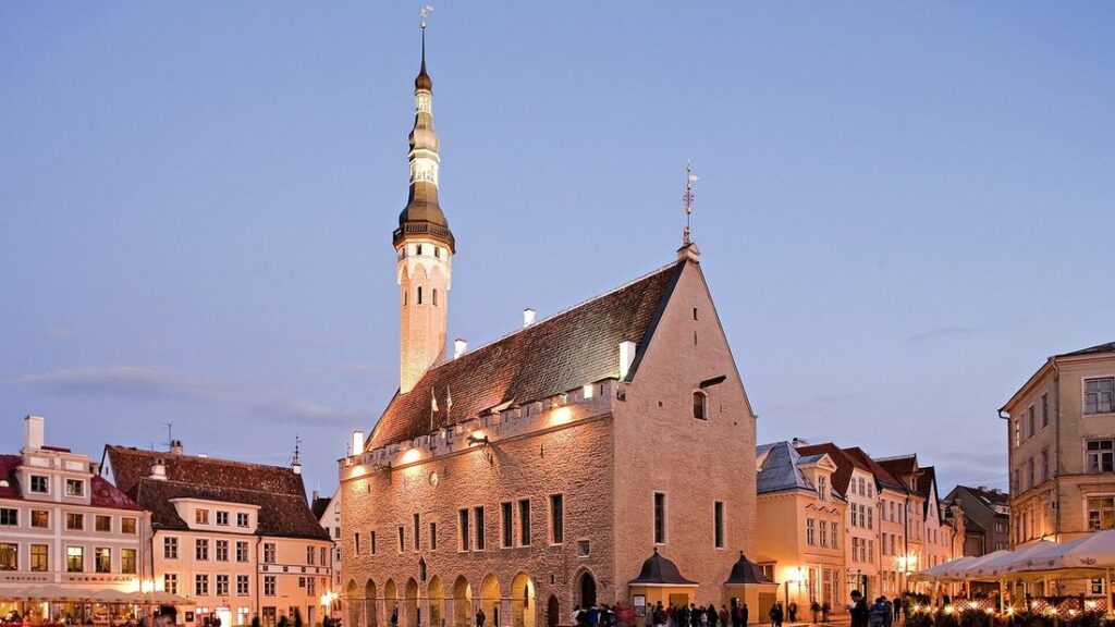 Hôtel de ville de Tallinn éclairé au crépuscule, sa flèche et son toit de tuiles, façades colorées autour de la place