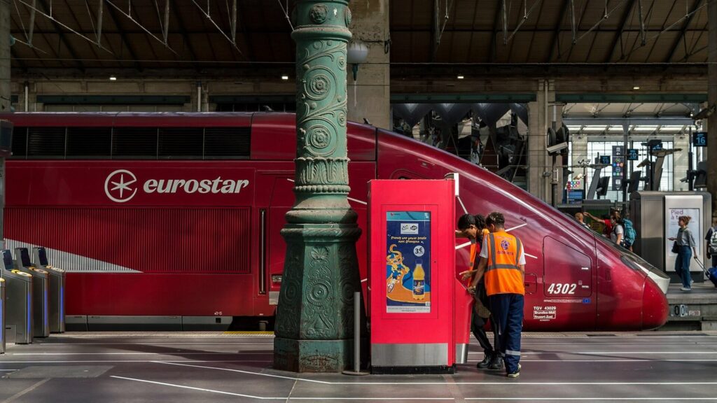 Rame rouge Eurostar à quai sous la halle métallique de la gare du Nord à Paris, avec deux agents en gilet orange près d'un poteau en fonte