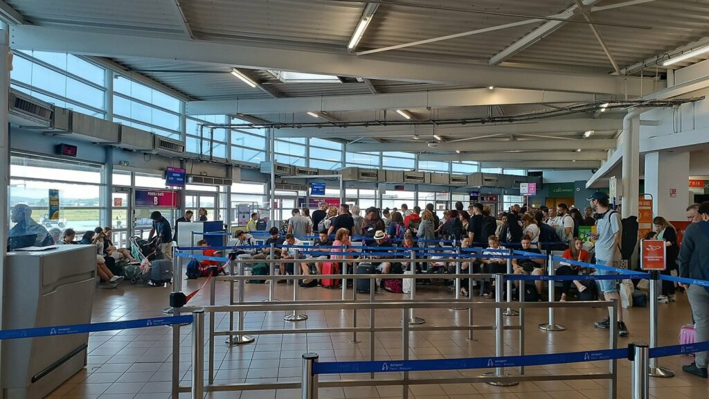 Hall de départ de l'aéroport de Beauvais-Tillé, avec une file de voyageurs derrière des barrières près de la porte d'embarquement B