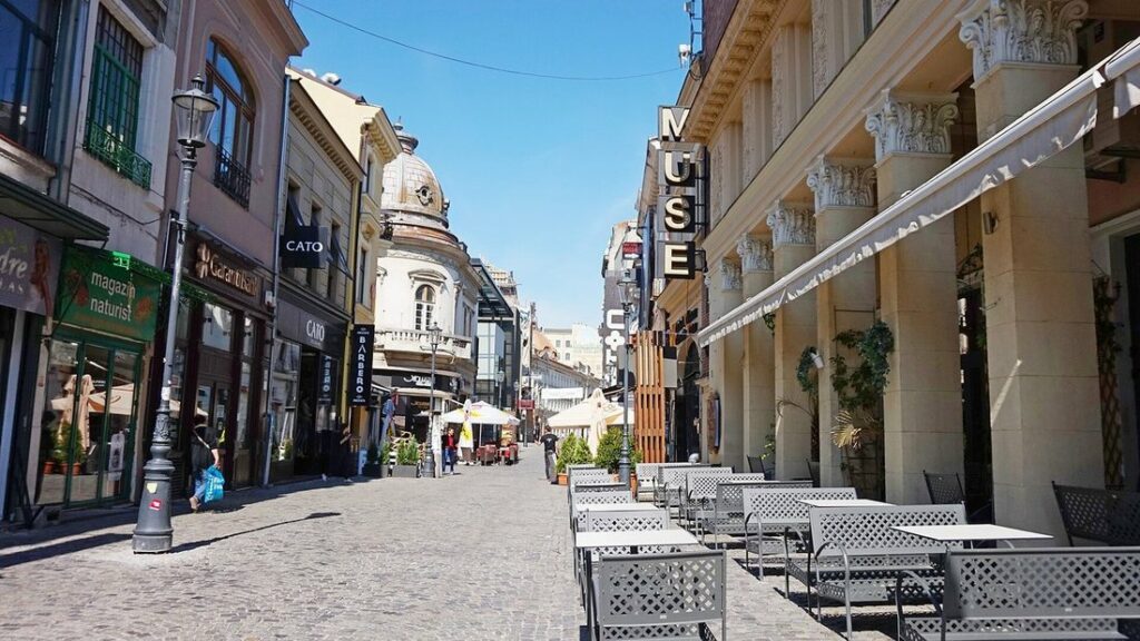 Rue pavée de Lipscani à Bucarest, avec des façades de commerces à gauche et une colonnade et des terrasses à droite