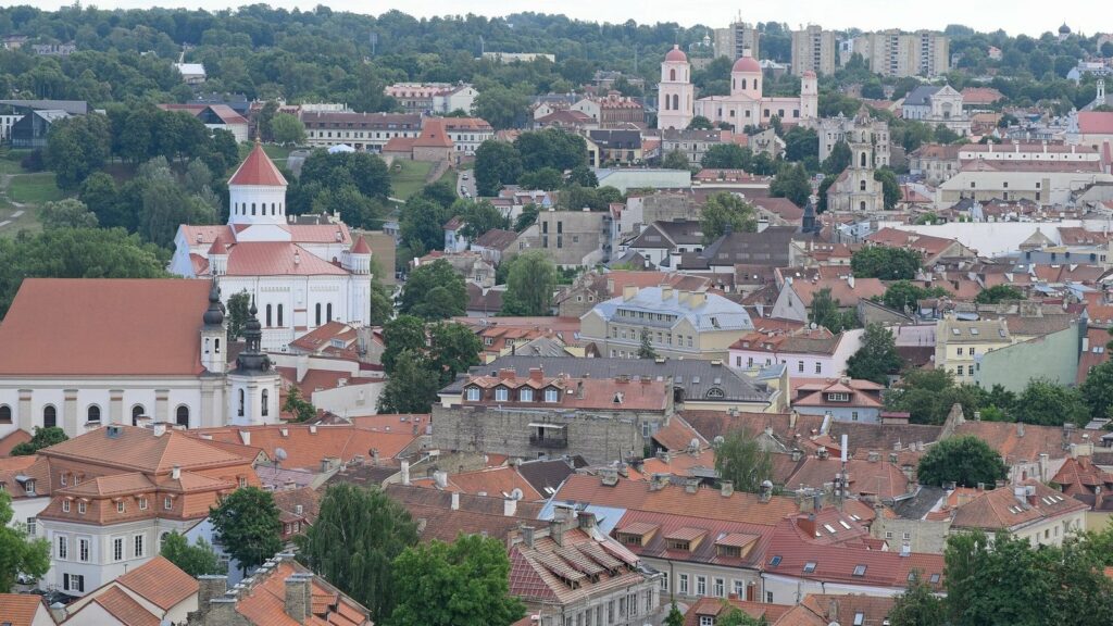 Toits de tuiles rouges et clochers de la vieille ville de Vilnius, vus d'en haut, avec des collines boisées au fond