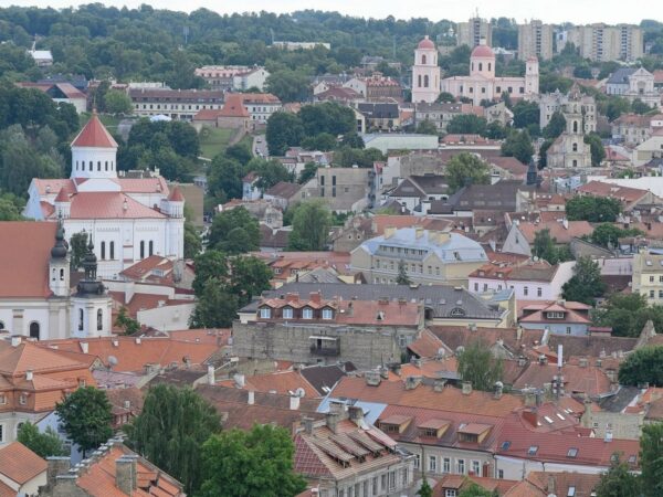 Toits de tuiles rouges et clochers de la vieille ville de Vilnius, vus d'en haut, avec des collines boisées au fond