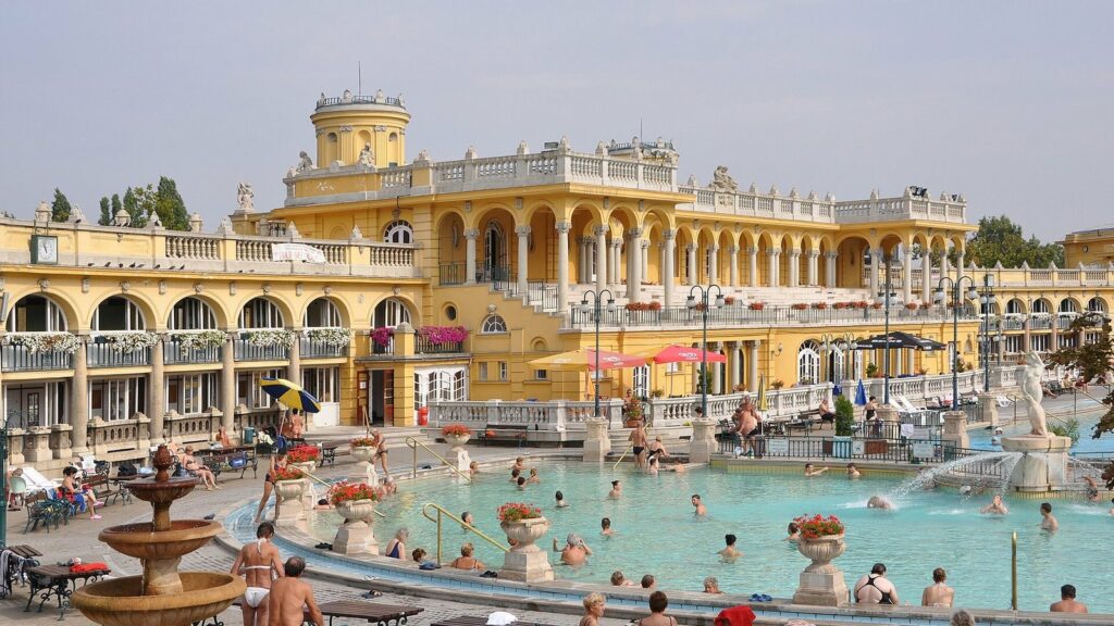 Façade jaune à colonnades des bains Széchenyi à Budapest, avec baigneurs dans le grand bassin extérieur