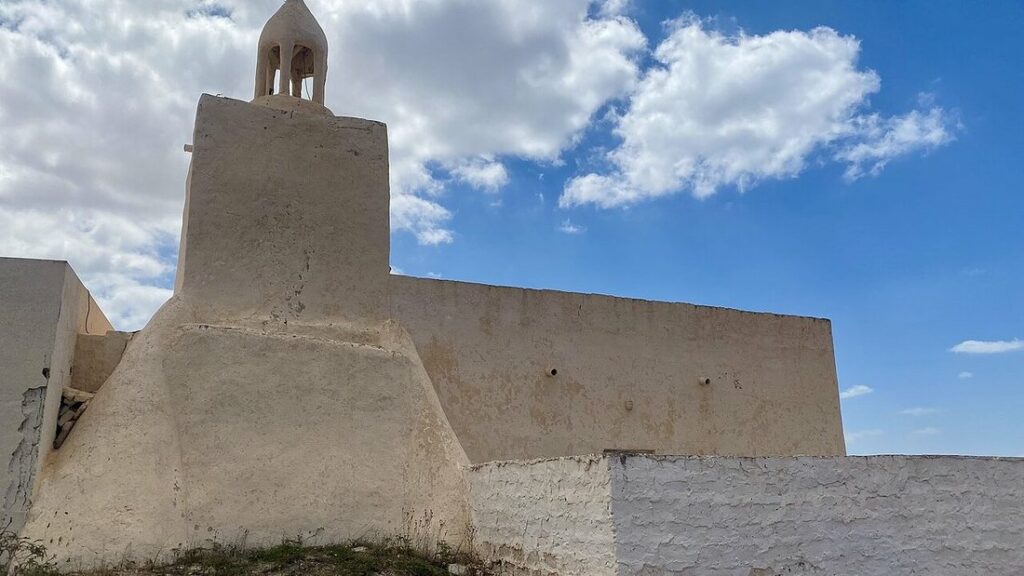 Mosquée aux murs crépis beiges et au petit minaret trapu sous un ciel bleu nuageux, à Djerba
