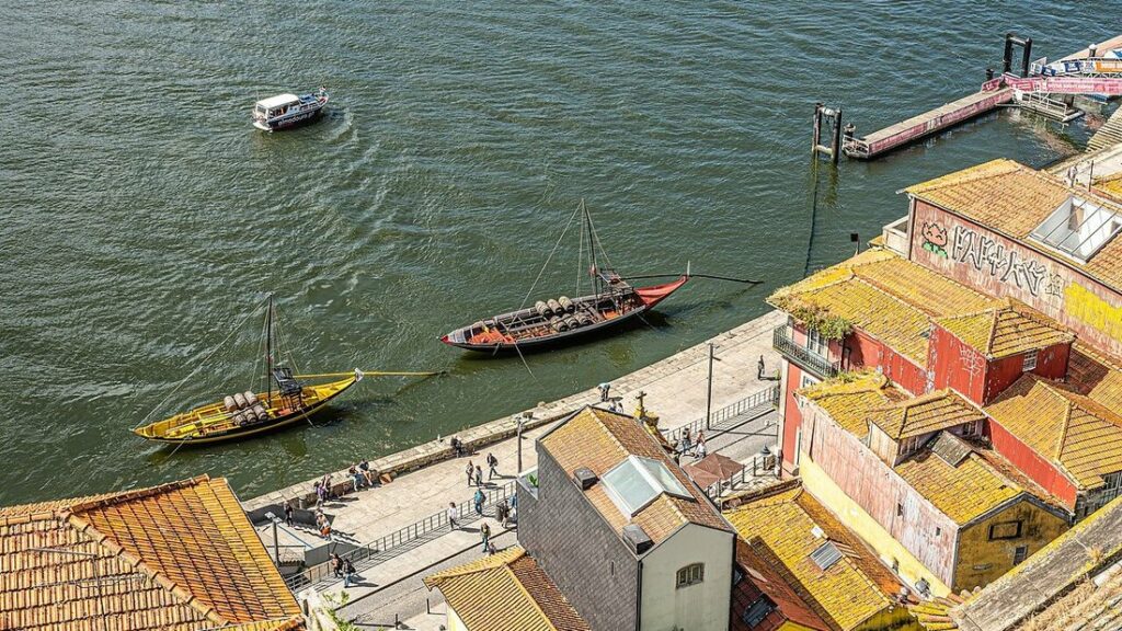 Quais du Douro à Porto vus d'en haut, avec deux bateaux traditionnels chargés de tonneaux et des toits de tuiles