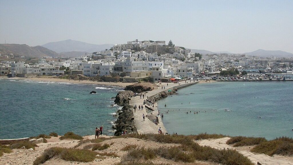 Ville blanche de Naxos étagée sur la colline, vue à travers la baie depuis une digue piétonne