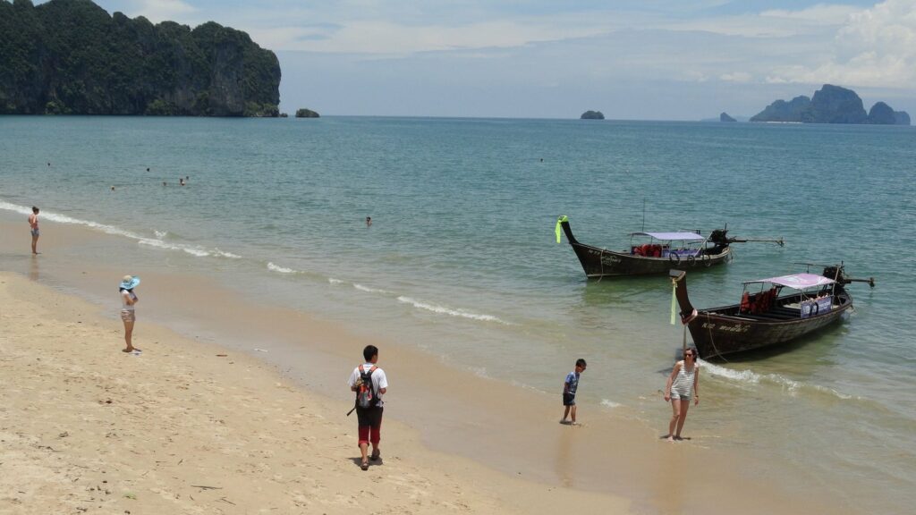 Plage de sable d'Ao Nang avec deux bateaux longtail au mouillage et des falaises boisées dans la baie