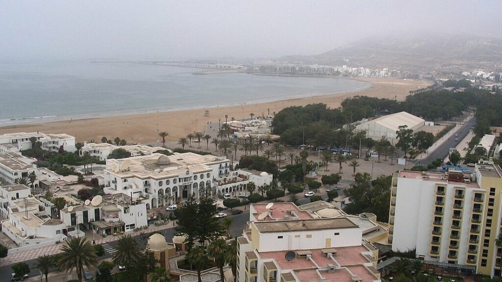 Vue plongeante sur la longue plage de sable d'Agadir, ses hôtels blancs et ses palmiers sous un ciel voilé