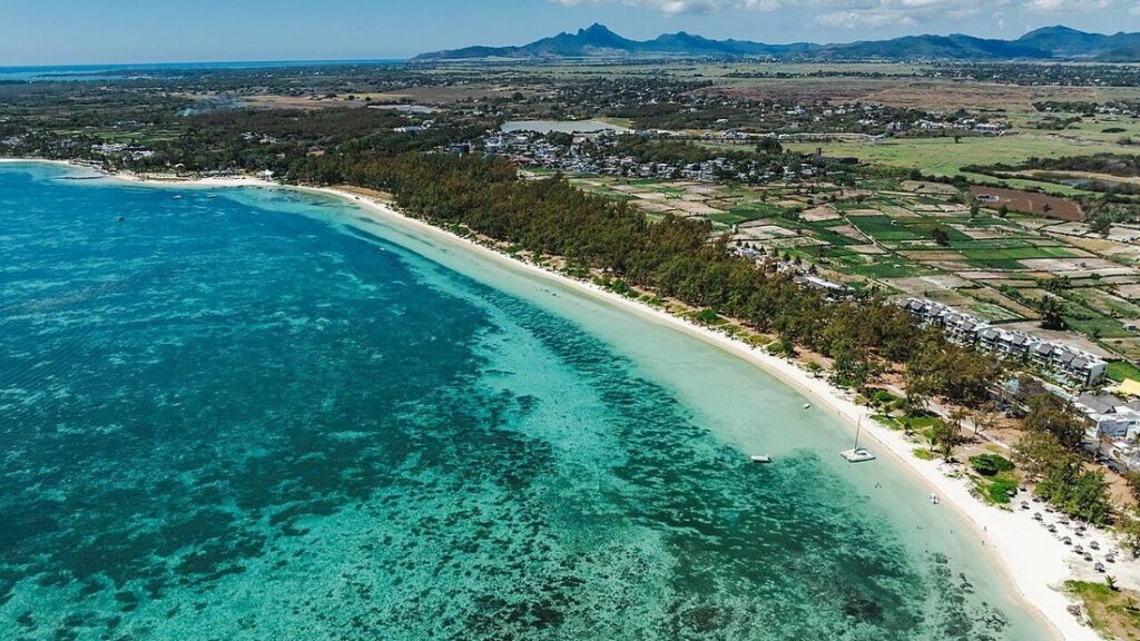 Vue aérienne d'un lagon turquoise bordé d'une plage blanche, d'arbres et de champs, à Belle Mare
