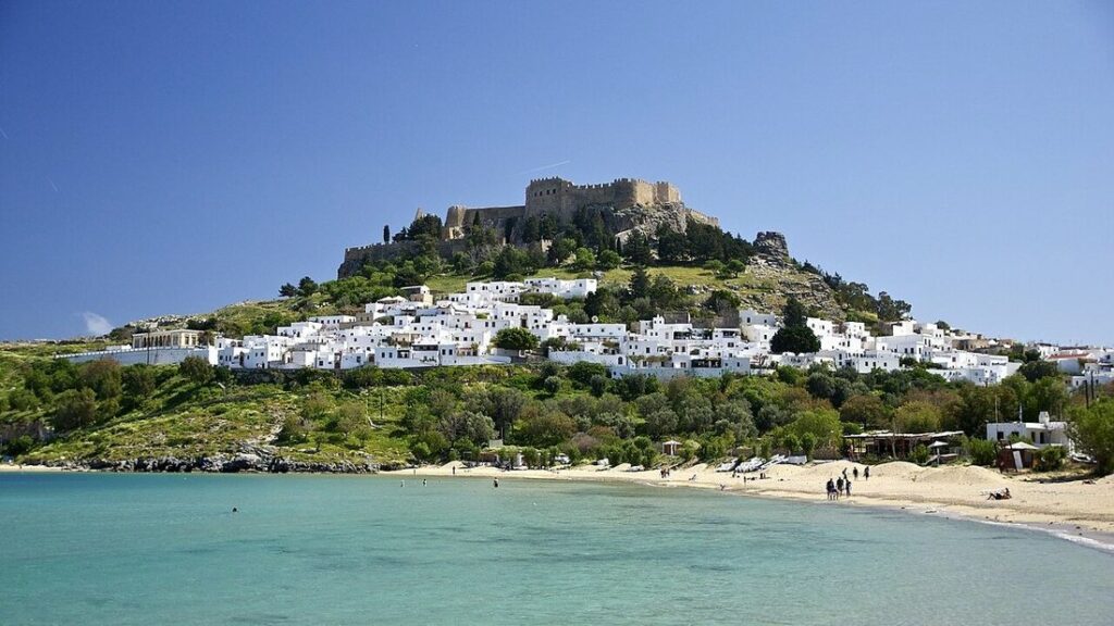 Village de maisons blanches sur une colline surmontée d'une forteresse, au-dessus d'une baie de sable à Lindos