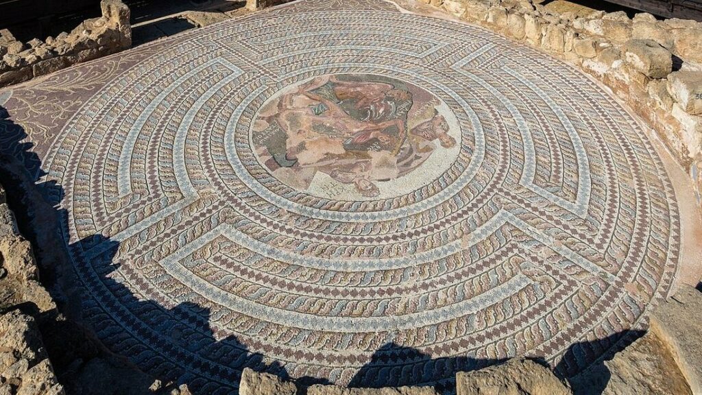 Grande mosaïque circulaire à motifs de labyrinthe et médaillon central, entourée de murs de pierre antiques