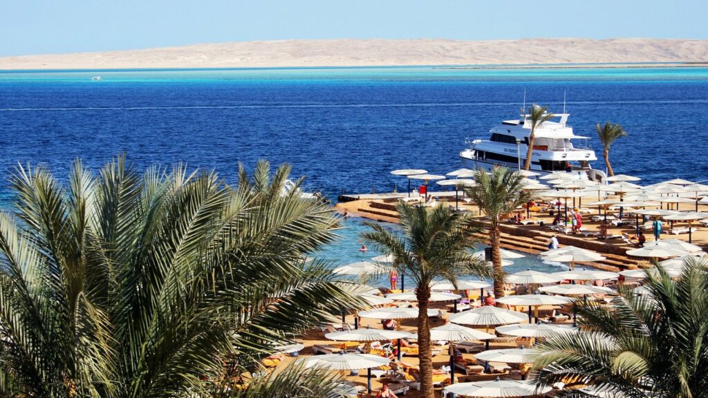 Plage d'hôtel à Hurghada avec palmiers, parasols blancs, un yacht au ponton et la mer Rouge d'un bleu profond