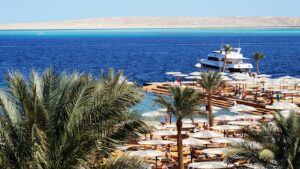 Plage d'hôtel à Hurghada avec palmiers, parasols blancs, un yacht au ponton et la mer Rouge d'un bleu profond
