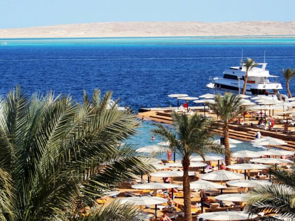 Plage d'hôtel à Hurghada avec palmiers, parasols blancs, un yacht au ponton et la mer Rouge d'un bleu profond