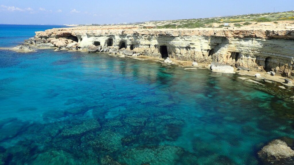 Falaise claire percée de petites grottes au-dessus d'une eau transparente, turquoise et verte, au cap Gréco à Chypre