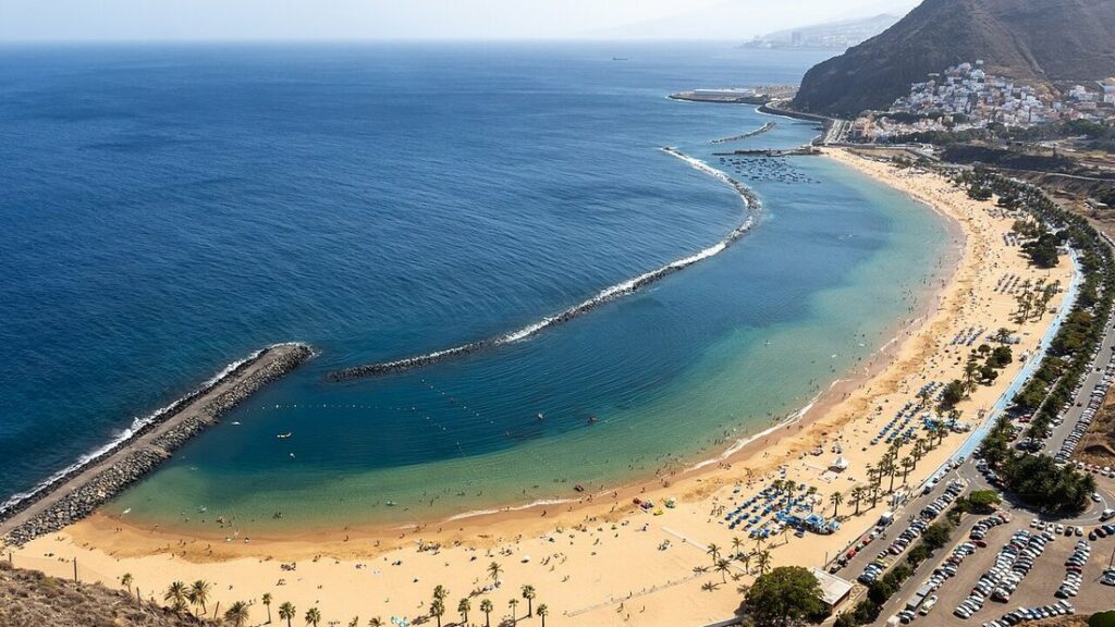Plage de sable doré en arc de cercle protégée par une digue, au pied d'une montagne, à Las Teresitas