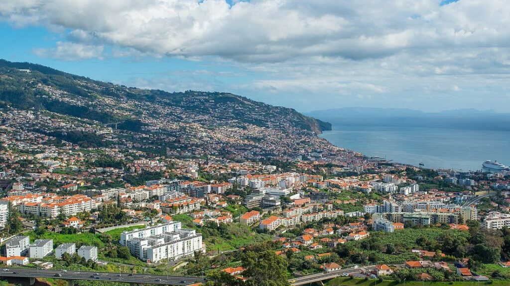 Maisons blanches aux toits orange sur une colline verte qui descend vers l'océan, vue sur Funchal à Madère