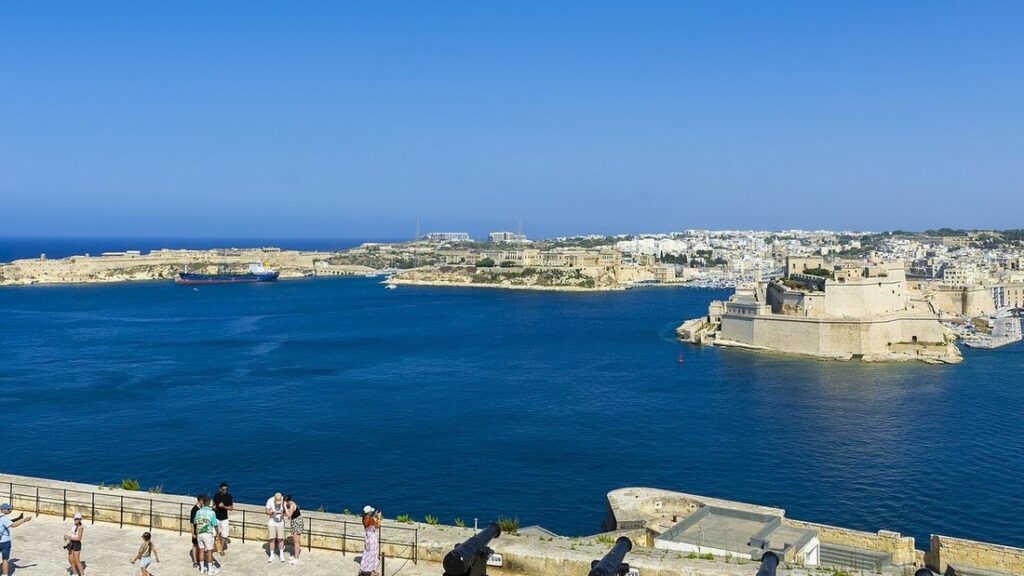 Vue sur le Grand Port de La Valette, eau bleu profond, fortifications de pierre claire et canons au premier plan