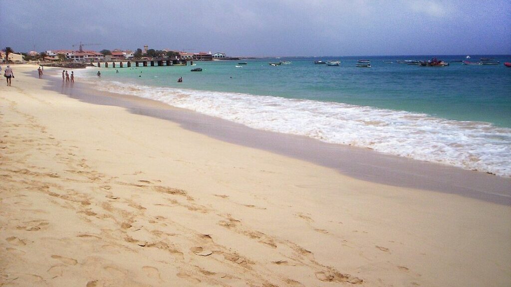 Plage de sable clair léchée par des vagues d'écume, bateaux au large, à Santa Maria sur l'île de Sal
