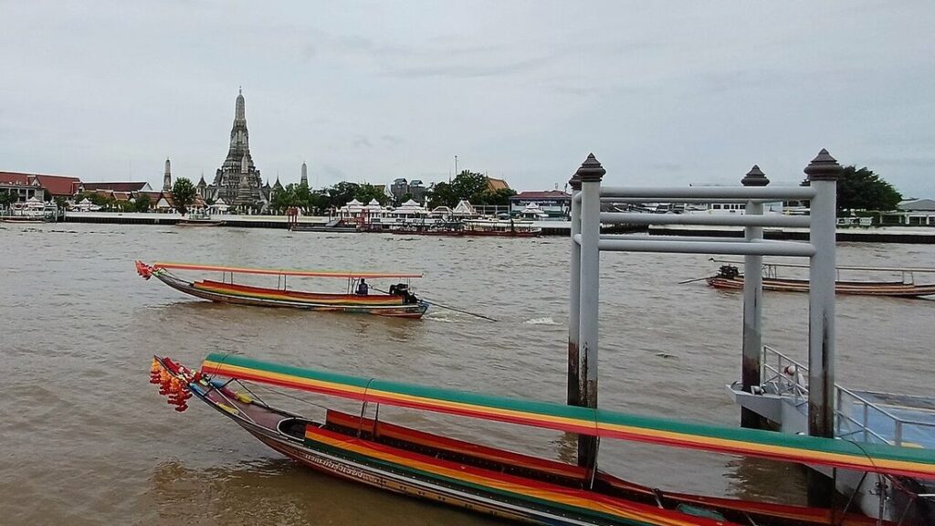 Fleuve brun avec des bateaux à longue queue colorés, un embarcadère et le temple Wat Arun au fond, à Bangkok