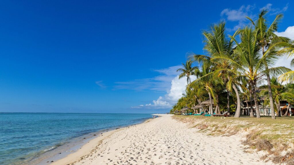 Plage de sable blanc bordée de cocotiers, lagon turquoise et ciel bleu à Le Morne, île Maurice