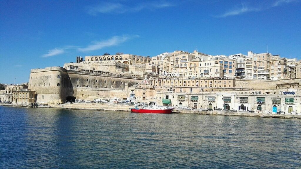 Bastion fortifié et façades de pierre claire au bord de l'eau calme du Grand Port, avec un petit bateau rouge