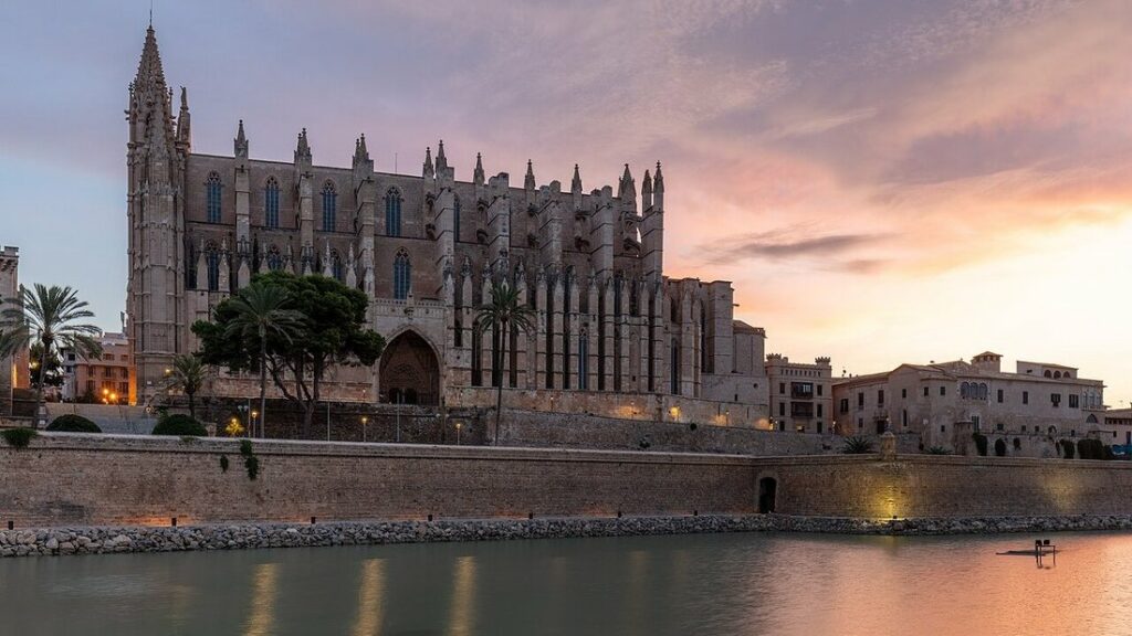 Cathédrale gothique de Palma éclairée au crépuscule, derrière un mur de pierre et un plan d'eau calme