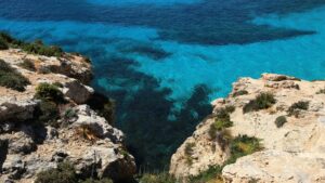Eau turquoise vue du haut d'un rebord rocheux couvert de végétation basse, sur l'île de Comino, à Malte