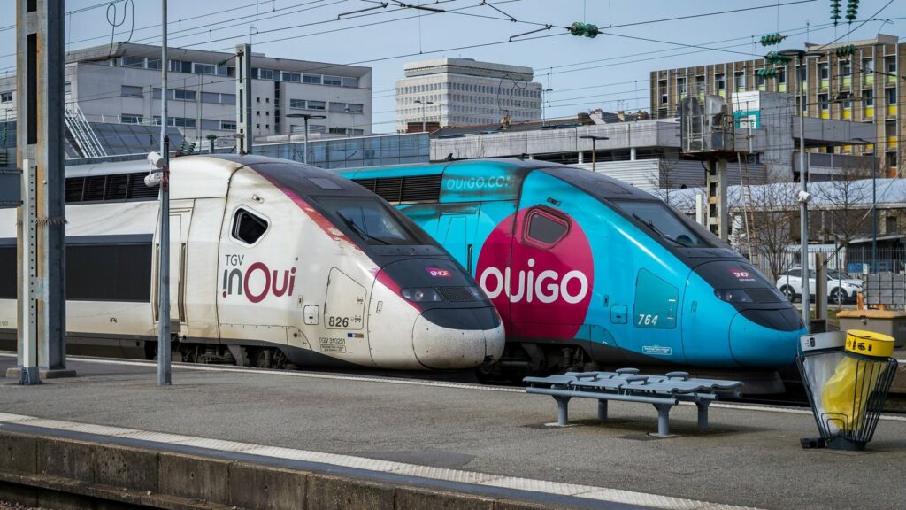 Deux rames de TGV côte à côte à quai, l'une blanche marquée TGV inOui, l'autre bleue et rouge marquée Ouigo